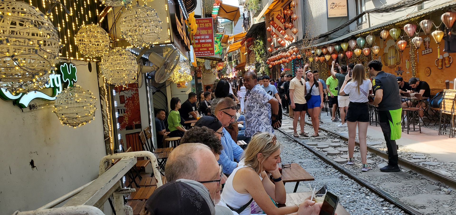 Tourists enjoying Hanoi Train Street with beers and colorful lanterns along the railway tracks in Vietnam.