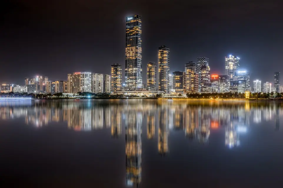This image captures a stunning night view of Hong Kong’s skyline. that reflect beautifully on the surface of Victoria Harbour in the foreground.