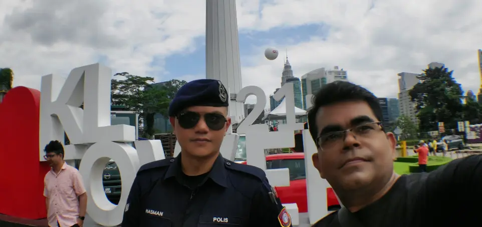 AJ Backpacker is taking a selfie with a policeman in front of the KL Tower (Kuala Lumpur Tower) signage in Malaysia.